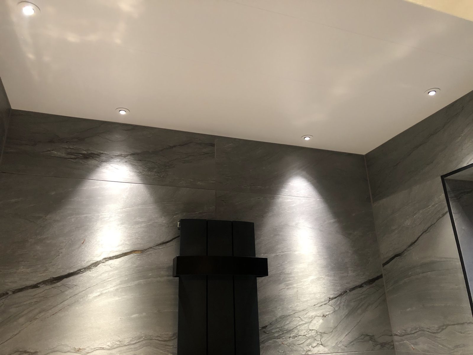 Dark marble wall washed by ceiling spotlights with a black radiator