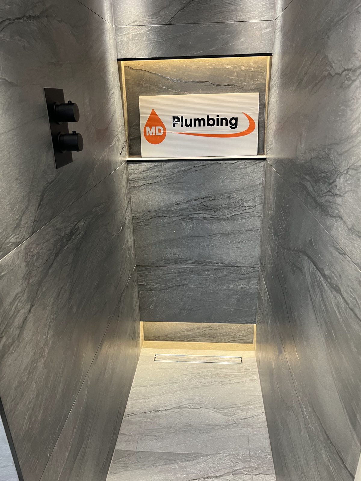Walk-in shower with a lit recessed niche and grey stone-effect tiles