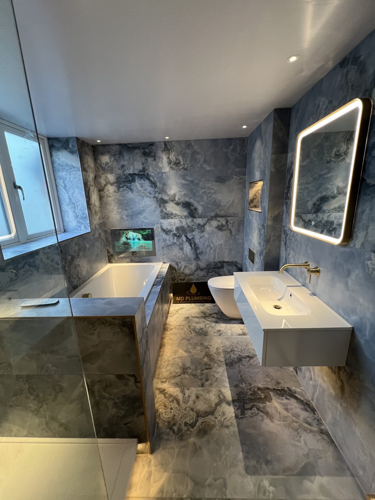 Large bathroom in dark marble with a built-in television and brass taps