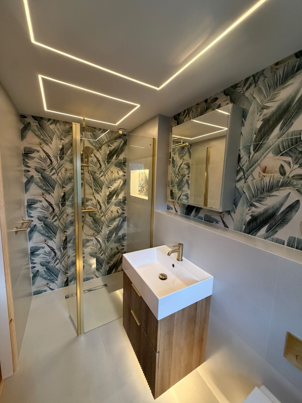 Shower room with tropical leaf wallpaper, a brass-framed screen and a timber vanity